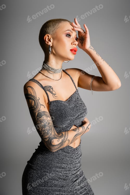 Preview: tattooed woman with short hair and red lips holding hand near face and posing in glamour clothes