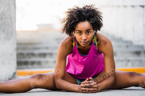 Preview: Afro athlete woman stretching legs before exercise.