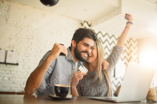 Preview: Happy couple doing online shopping through laptop and credit card at cafe.