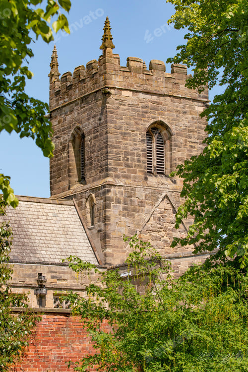 Aperçu: a tall brick building next to trees and bushes on the ground