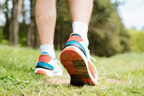 Preview: Hiking on summer day, outdoors. Man walking in nature, close-up of red sports sneakers. Dirty boot