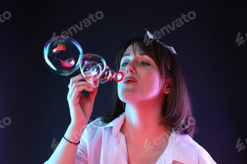 Preview: Portrait of happy woman blowing bubbles on dark background