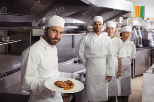 Preview: Smiling chef holding delicious dish in kitchen