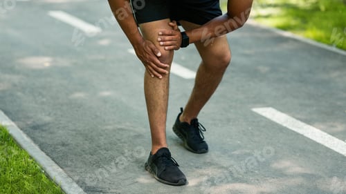 Preview: Closeup view of black guy suffering from knee pain after sports injury at jogging track
