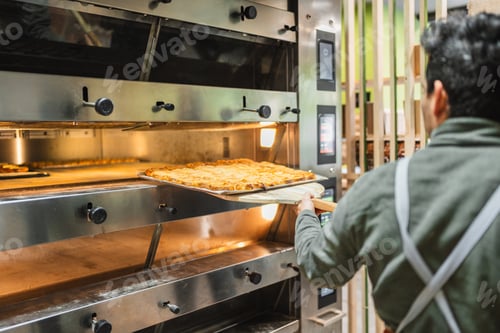 Preview: Baker taking freshly baked bread out of oven in bakery