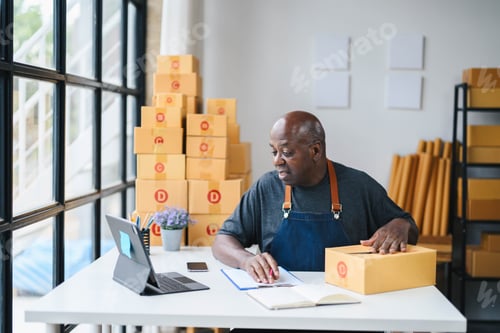 Preview: Senior Man Working on Online Business from Home Office with Cardboard Boxes, Laptop, and Notepad,