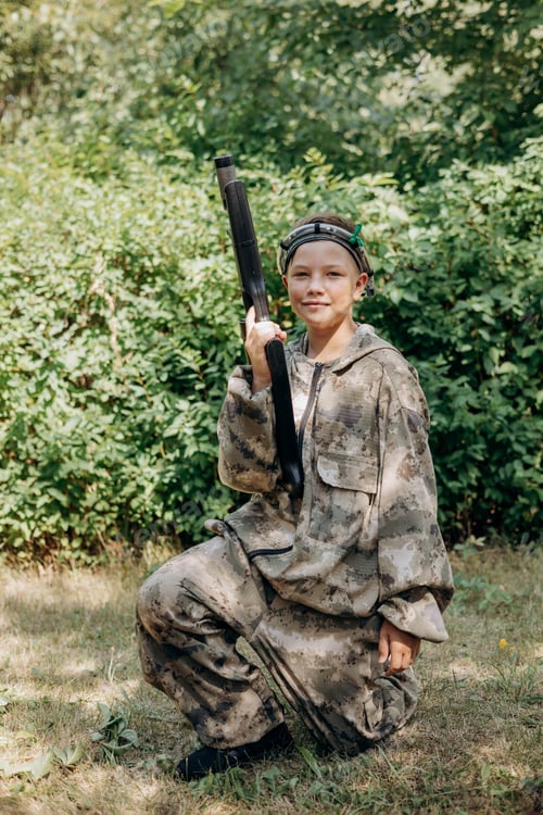 Preview: Boy with a weapon in his hand playing laser tag shooting game in outdoor. War simulation game