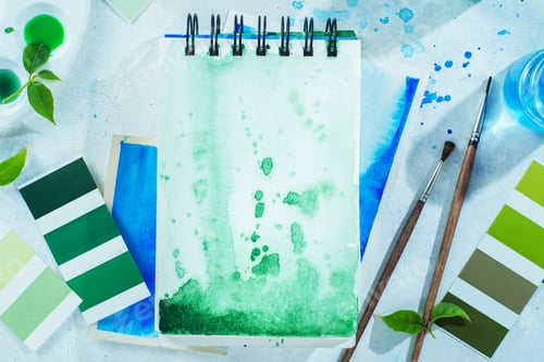 Preview: Artist workplace with tools and plants, green and blue watercolor sketchbooks, brushes and color