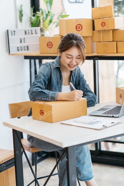 Preview: Asian woman entrepreneur is packing product to the box at home workplace. teenager business owner wo