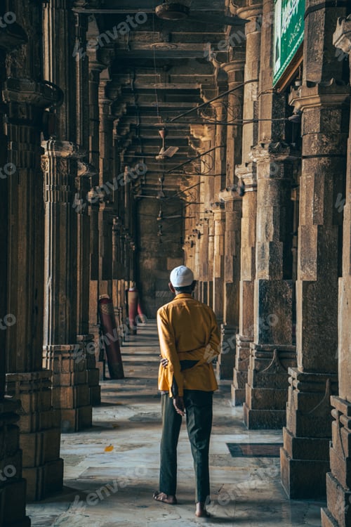 Preview: Vertical shot of a man wearing a yellow jacket, facing towards the columns of a building