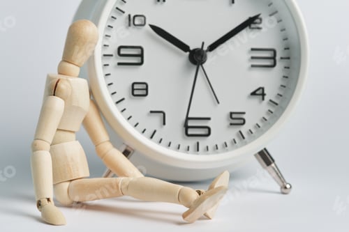 Preview: Wooden man sits near alarm clock. Concept of being late, long wait, transience of time, old age.