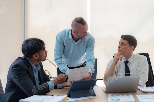 Preview: Group of diverse businessman going over paperwork together and working on laptop at meeting.