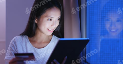 Preview: Woman shopping on tablet computer with credit card at night
