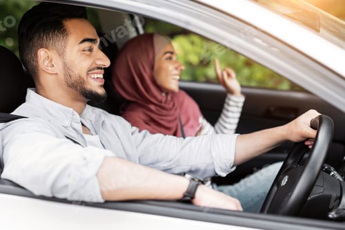 Preview: Glad smiling millennial islamic husband driving at steering wheel with wife in hijab, ride in car