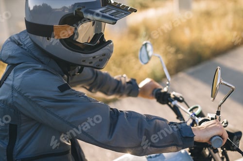 Preview: A motorcycle rider in a helmet sits on a motorcycle on the road against the sunset.