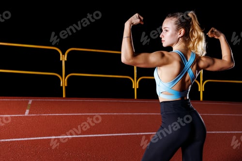 Preview: Young athletic sportswoman posing with her muscles at the running track