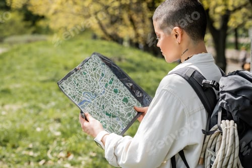 Preview: Young short haired and tattooed female hiker in casual clothes with backpack and travel equipment