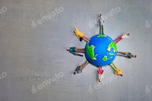 Visualização: Um grupo de pessoas de brinquedo em miniatura em várias cores está ao redor de um globo em uma superfície cinza.