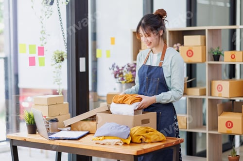 Preview: Startup SME small business entrepreneur of freelance Asian woman wearing apron using laptop and box