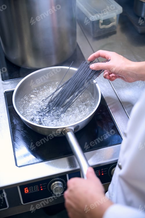 Preview: Cook puts a portion of black spaghetti into boiling water