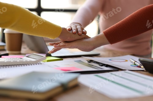 Preview: Coworkers gather around and hold hands in the workplace.