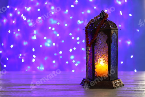 Preview: Muslim lamp with candle on table against blurred fairy lights. Fanous as Ramadan symbol