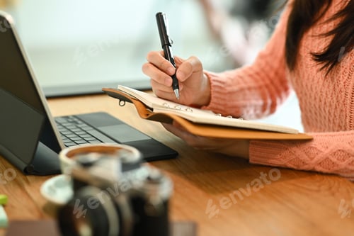 Preview: Cropped shot young woman holding pen and writing her diary.