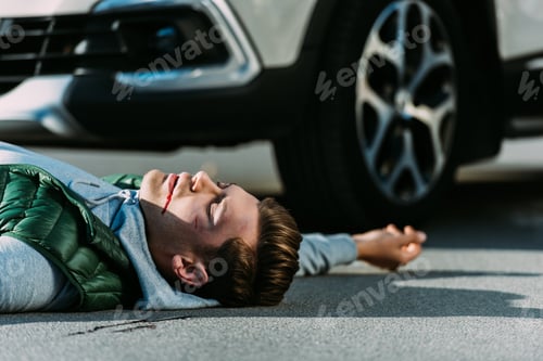 Preview: side view of injured young man lying on road after traffic collision