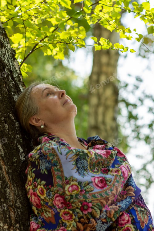 Preview: Portrait of an elderly woman in an elegant scarf in the open air against the background of a birch f