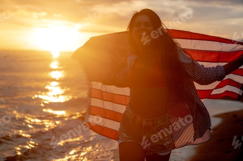 Preview: Young woman holding national American flag walking ocean beach. America Independence Day concept