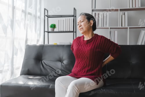 Preview: Elderly asian housewife woman sitting on sofa. Back pain, lumbar pain, cervical spine