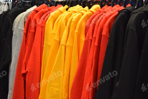 Preview: Closeup of solid-colored hoodies on a rack at a store under the lights