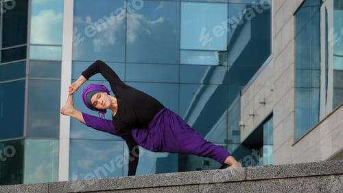Preview: Strong woman in hijab flexible girl doing yoga exercises on street city building background sport
