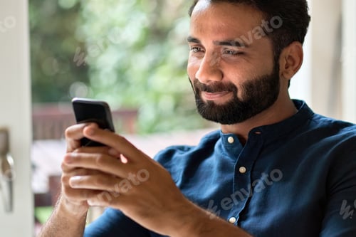 Preview: Indian man holding smartphone using mobile phone at home.