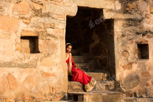 Preview: Indian woman in red saree sitting on stairs.
