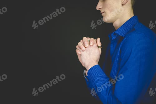 Preview: Male wearing a blue t-shirt praying with a black background