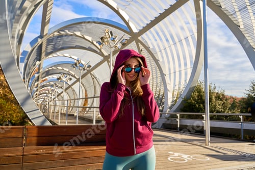 Preview: Sporty woman adjusting sunglasses on modern bridge in madrid rio park