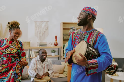 Preview: Young Black Man Playing Drum While Celebrating Kwanzaa with Friends Indoors