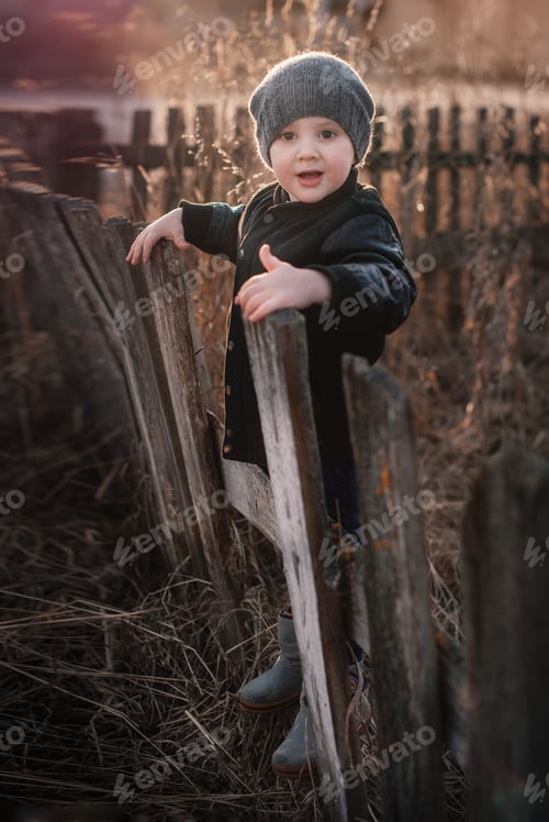Preview: little boy in the village, on an old wooden fence
