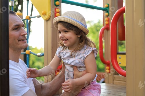 Preview: A cute little girl plays and has fun with her dad on the playground on bright and colorful rides