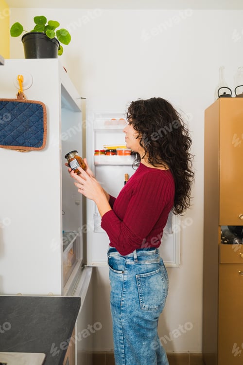 Preview: Young woman choosing food from home refrigerator