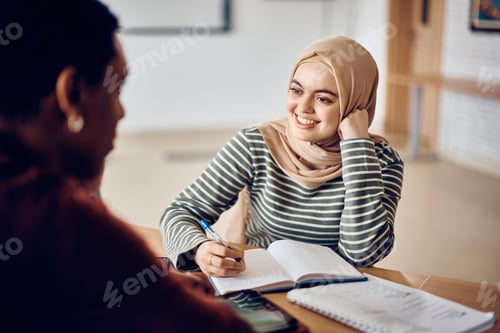 Preview: Young happy Muslim student talking to her classmate in the classroom.