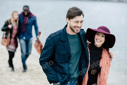 Preview: Young people having pleasant stroll on river beach. Smiling couple on foreground