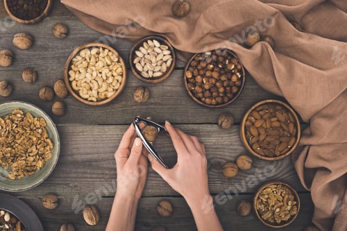 Preview: top view of person cracking walnut with nutcracker above wooden table