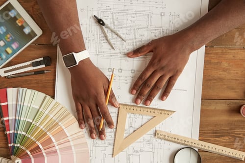 Preview: Architect working on a blueprint. Top view of afro american man drawing something on a blueprint
