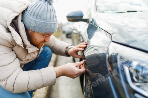 Preview: Examining the damage a man looks at a car with scratches,