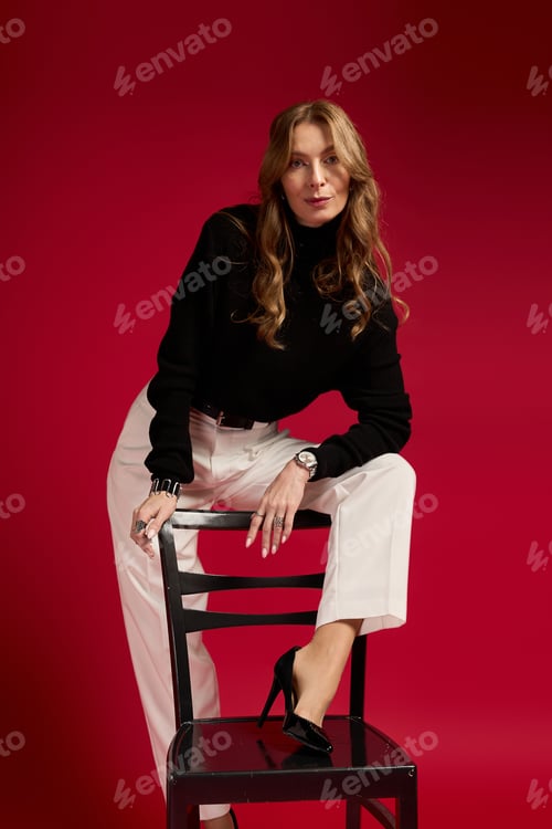 Preview: Elegant woman in stylish outfit poses confidently against a vivid red backdrop