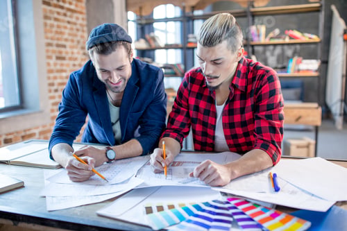 Preview: Two young male architects holding pencils and discussing blueprints