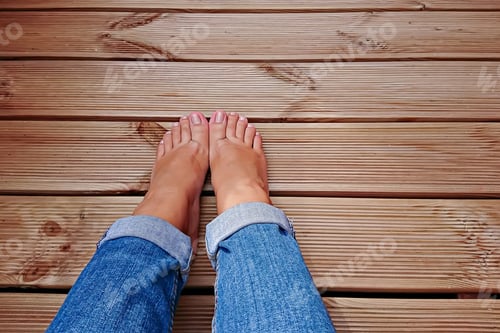Preview: View of woman's barefoot legs wearing blue jeans on wooden floor
