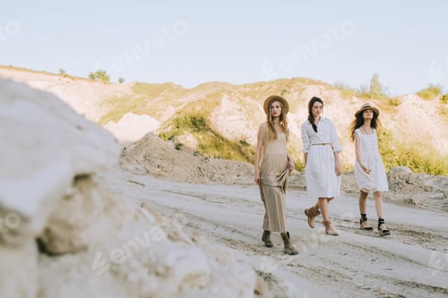 Preview: attractive stylish girlfriends in straw hats walking in sandy canyon
